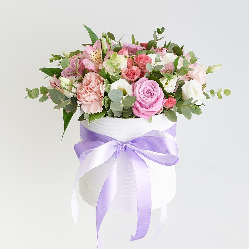 Floral arrangement in a box with a purple ribbon on a light gray background