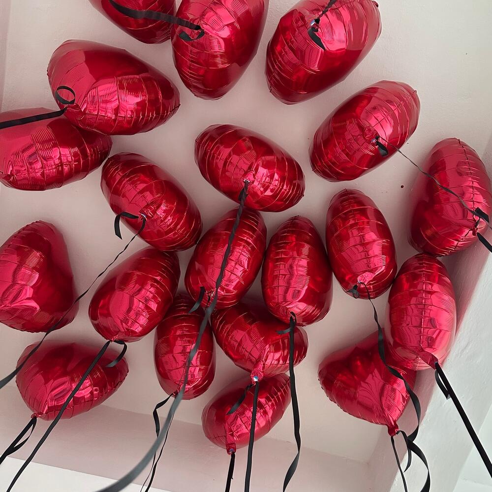 15 красных воздушных шаров в форме сердечек, подвешенных на атласных лентах к потолку.