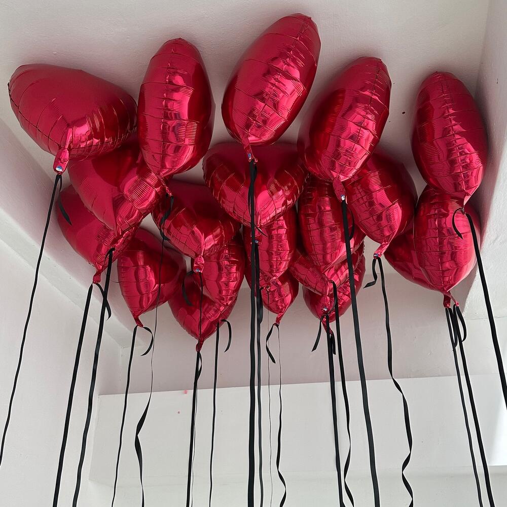 15 красных воздушных шаров в форме сердечек, подвешенных на атласных лентах к потолку.